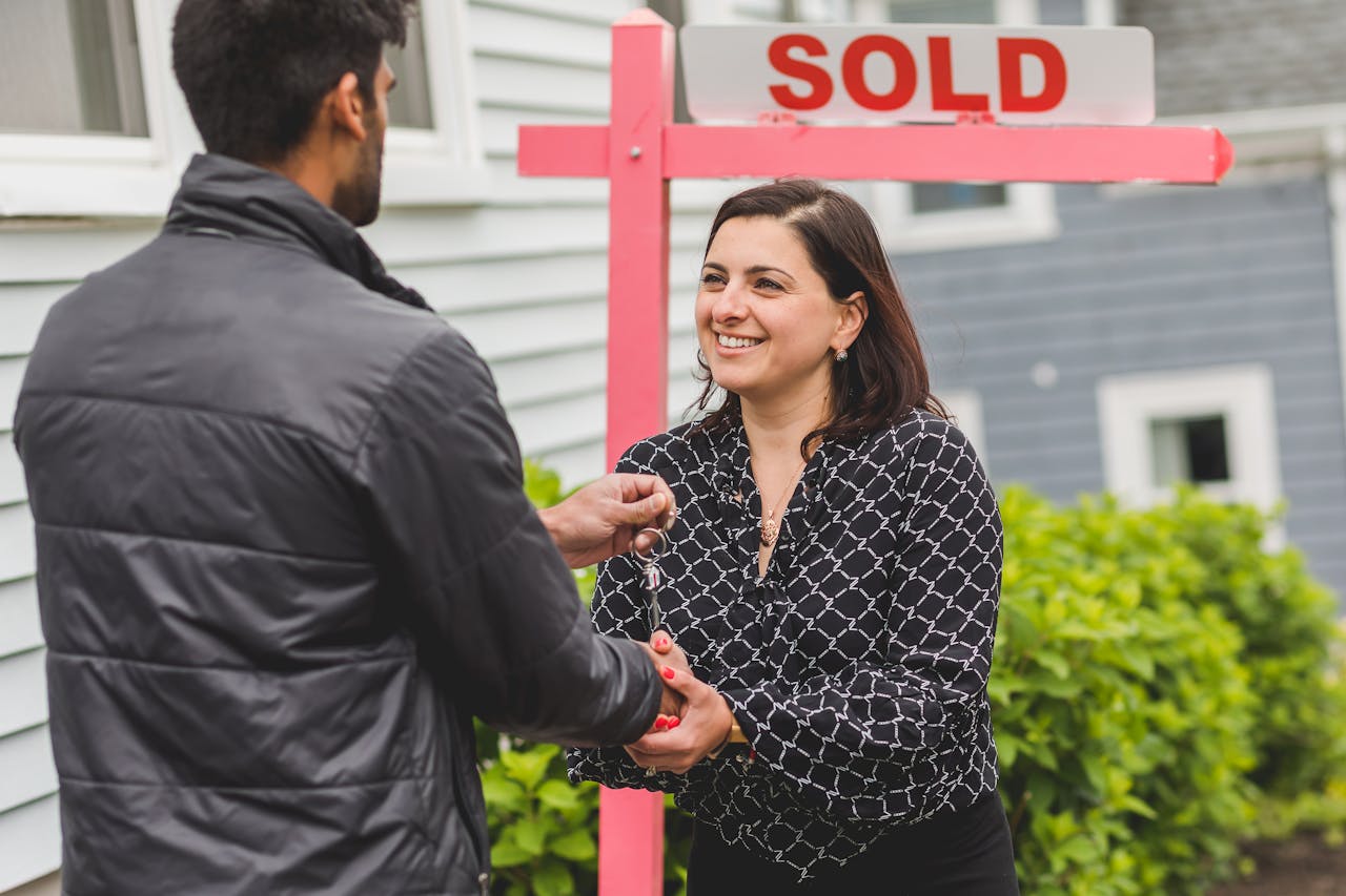 why-choose-us Real estate agent handing keys to a new homeowner with a 'Sold' sign in the background.
